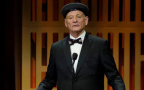 Bill Murray in a black suit and bowtie, wearing hat on stage