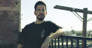 Mike Shinoda leaning on a railing wearing black tshirt