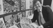 Neal Adams smiling at the camera holding a comic book