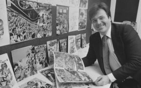 Neal Adams smiling at the camera holding a comic book
