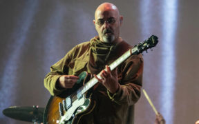 Paul Arthurs of Oasis in a green jacket playing guitar