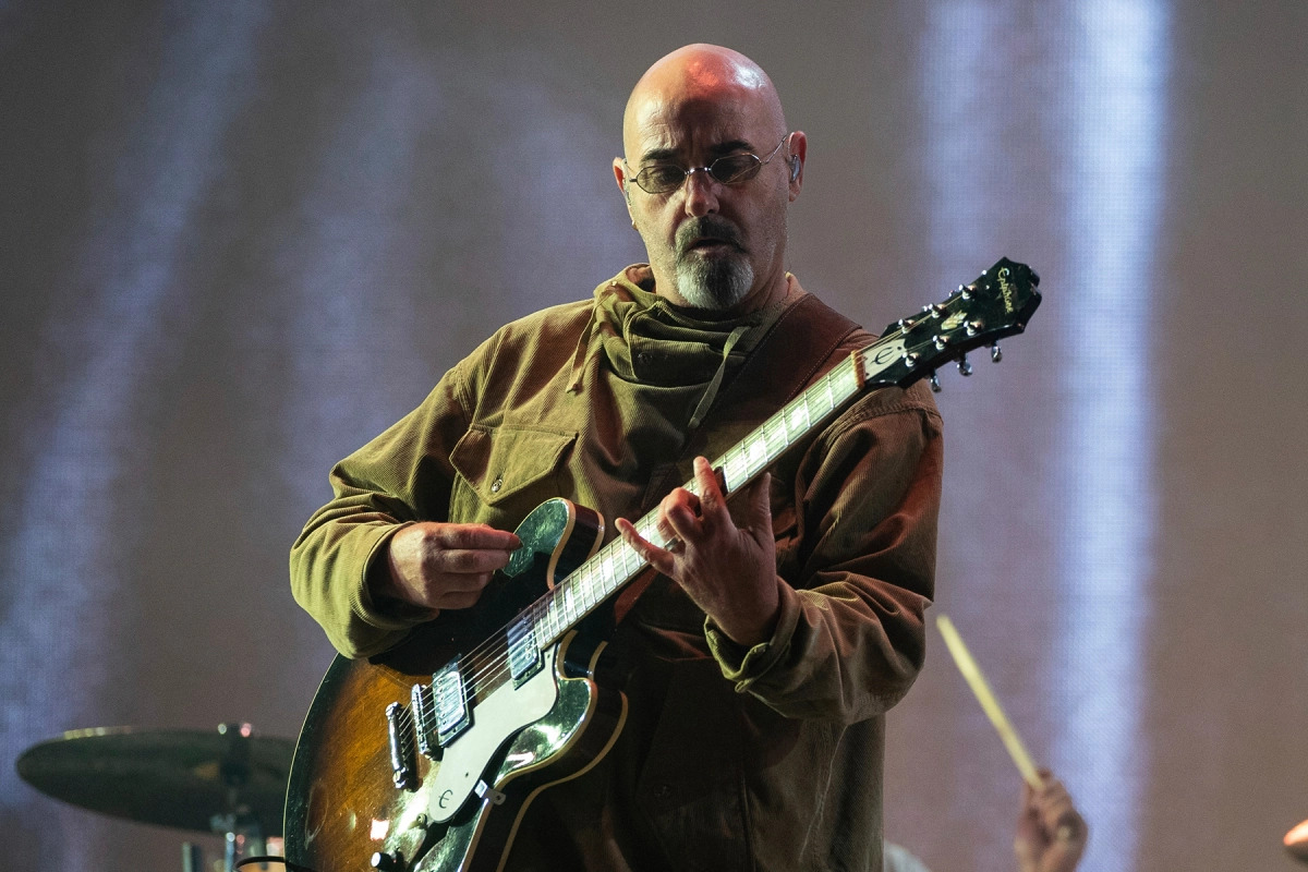 Paul Arthurs of Oasis in a green jacket playing guitar