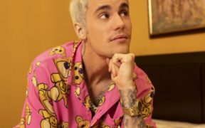 Justin Bieber in pink clothes, wearing gold watch hand on chin and looking up