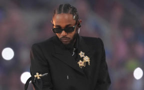 Kendrick Lamar in a black suit with gold wearing black sunglasses