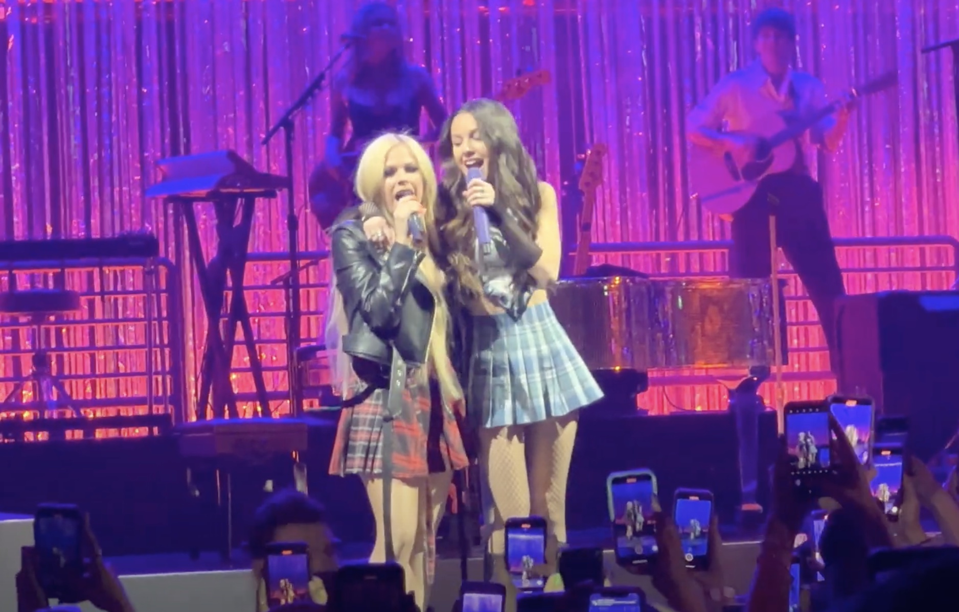 Avril Lavigne and Olivia Rodrigo wearing flannel plaid skirts and singing on stage