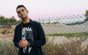 Karan Batta wearing a black jacket with a fence behind