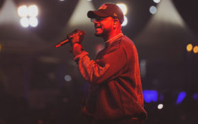 Desi hip-hop artist KING on stage singing into a microphone, wearing cap and sunglasses