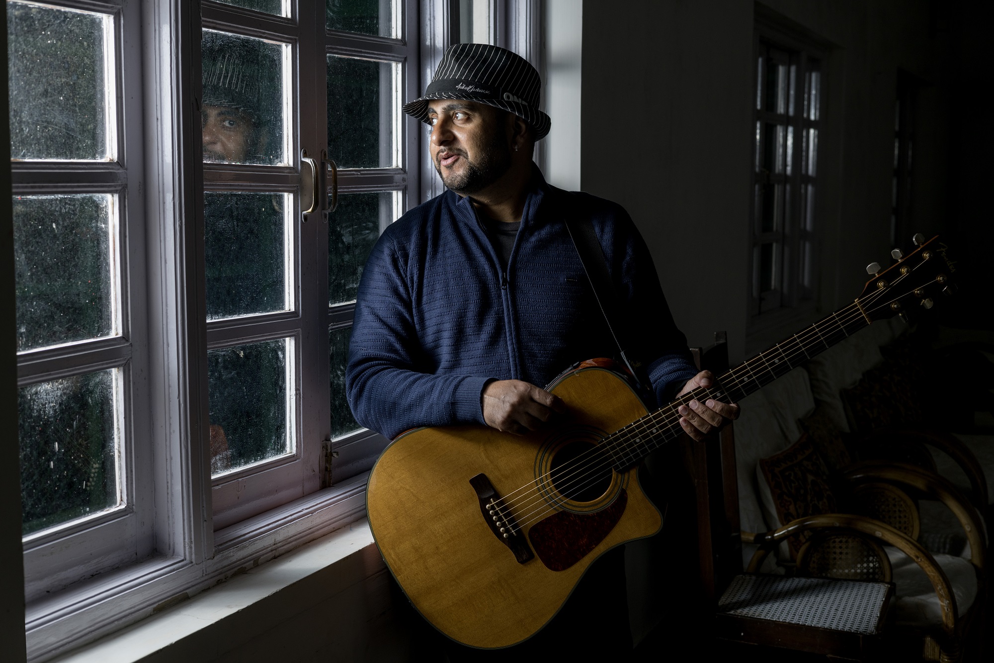 Singer-songwriter Rohan Solomon holding an acoustic guitar and staring out a window