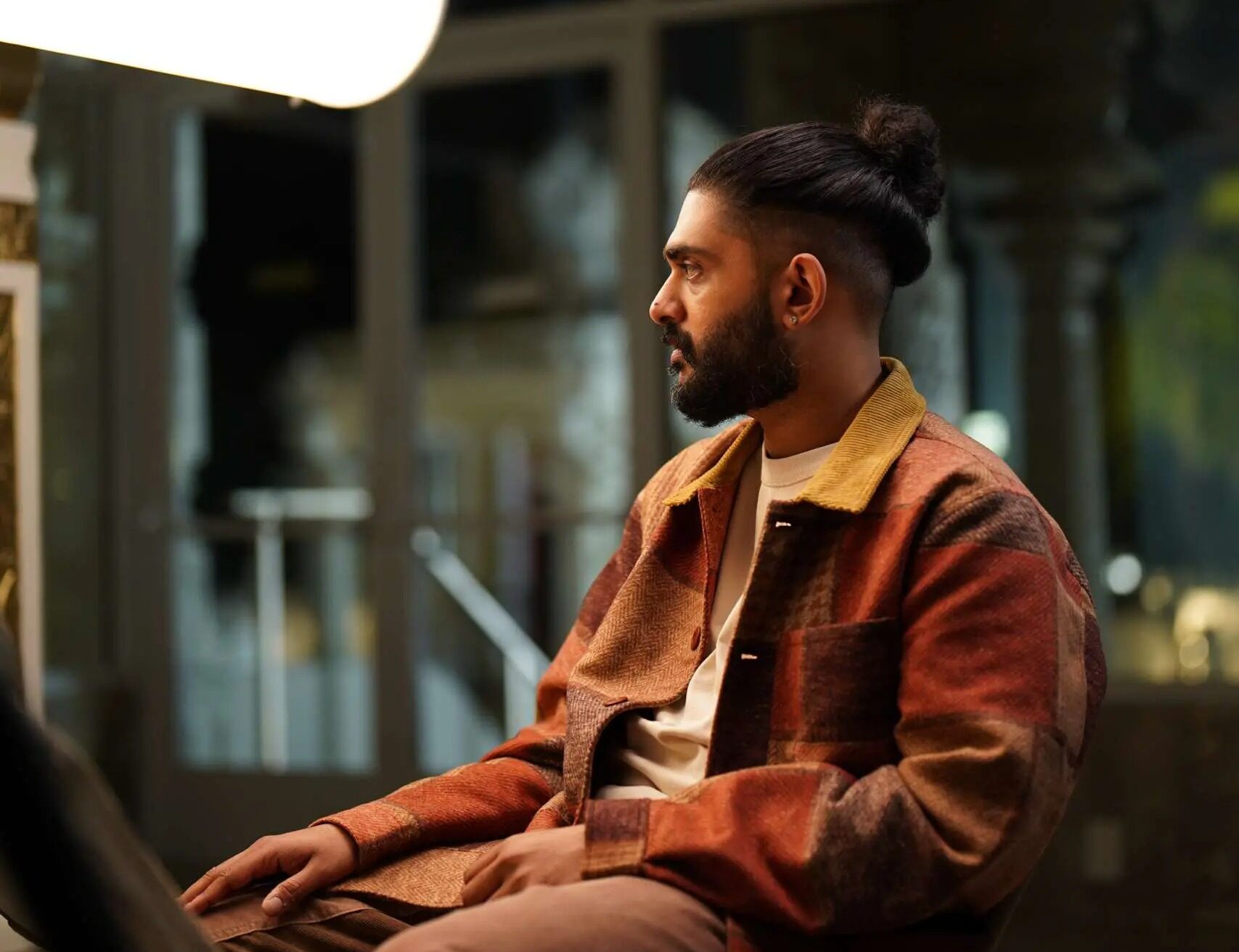 Sid Sriram in a brown jacket sitting under a light