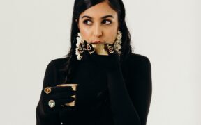 Singer and composer Aditi Ramesh dressed in a black top with black gloves and rings, sipping on a cup of filter coffee