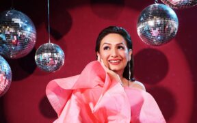 Singer Akriti Kakar smiling in a pink dress with disco balls in the background