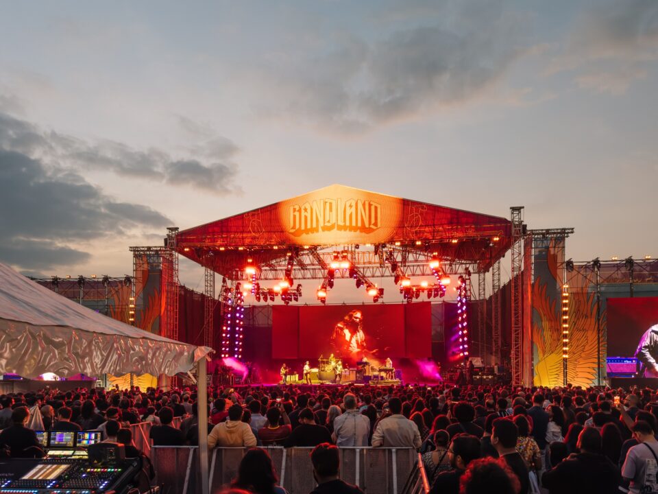 Crowd standing in front of a stage and cheering a band on screen