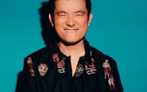 Actor Meiyang Chang grinning in a black print shirt