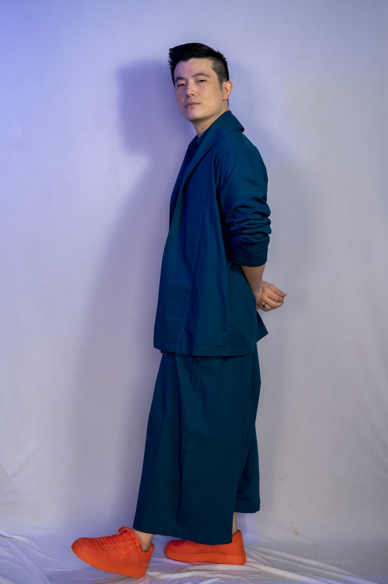 Meiyang Chang poses for a photo in a blue outfit, wearing bright red sneakers with his hands behind his back