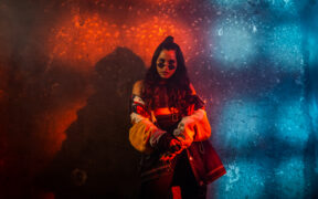 Singer Nikhita Gandhi wearing glasses and posing in red and blue light