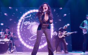 Singer Tanya Shanker on stage with band members in a black dress singing into a mic