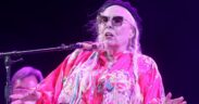 Joni Mitchell singing in dark glasses wearing red top