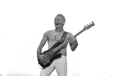 Sting in a black and white photo playing bass and singing on stage