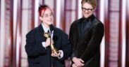 Billie Eilish and brother Finneas in black suits accepting Golden Globe award