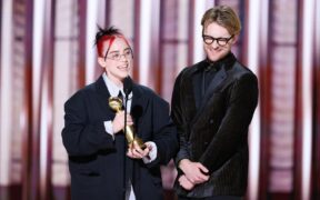 Billie Eilish and brother Finneas in black suits accepting Golden Globe award