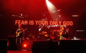 Rage Against the Machine performing on stage with the words 'Fear Is your only god' appearing on the screen in the background