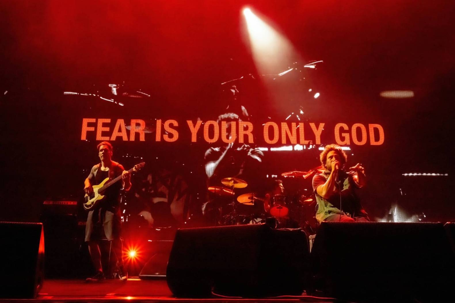 Rage Against the Machine performing on stage with the words 'Fear Is your only god' appearing on the screen in the background