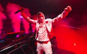 Alan Walker in white holding a mic in red light on stage