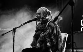 Kamal Singh aka Hoirong in a black and white photo wearing a cap and singing into mic with guitar