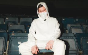 Alan Walker wearing all white seated on a chair