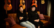 Allen Ling and Dave Lopez sitting on a couch surrounded by guitars