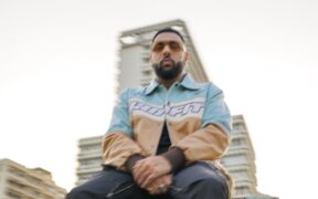 Badshah sitting at a height wearing blue and cream jacket with sunglasses
