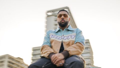 Badshah sitting at a height wearing blue and cream jacket with sunglasses