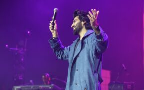 Singer Laqshay Kapoor in a blue shirt raising his hands with a mic