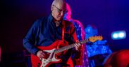 Guitarist Mark Knopfler playing a red guitar in a blue shirt