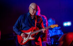Guitarist Mark Knopfler playing a red guitar in a blue shirt