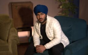 Singer Gurman in a white jacket and blue turban sitting on a blue sofa