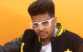 Music producer Hiten wearing white glasses and black and yellow jacket