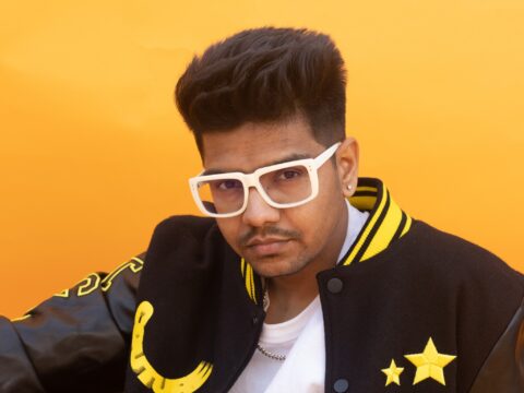 Music producer Hiten wearing white glasses and black and yellow jacket