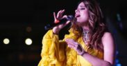 Punjabi singer Jyotica Tangri in a yellow dress singing into a mic at a concert