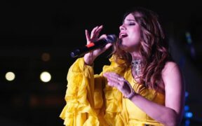 Punjabi singer Jyotica Tangri in a yellow dress singing into a mic at a concert