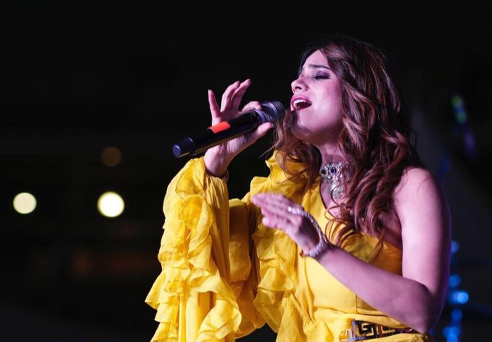 Punjabi singer Jyotica Tangri in a yellow dress singing into a mic at a concert