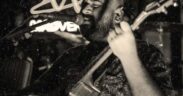 Black and white photo of Shourya Malhotra singing into a mic while playing guitar