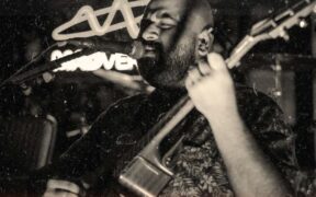 Black and white photo of Shourya Malhotra singing into a mic while playing guitar