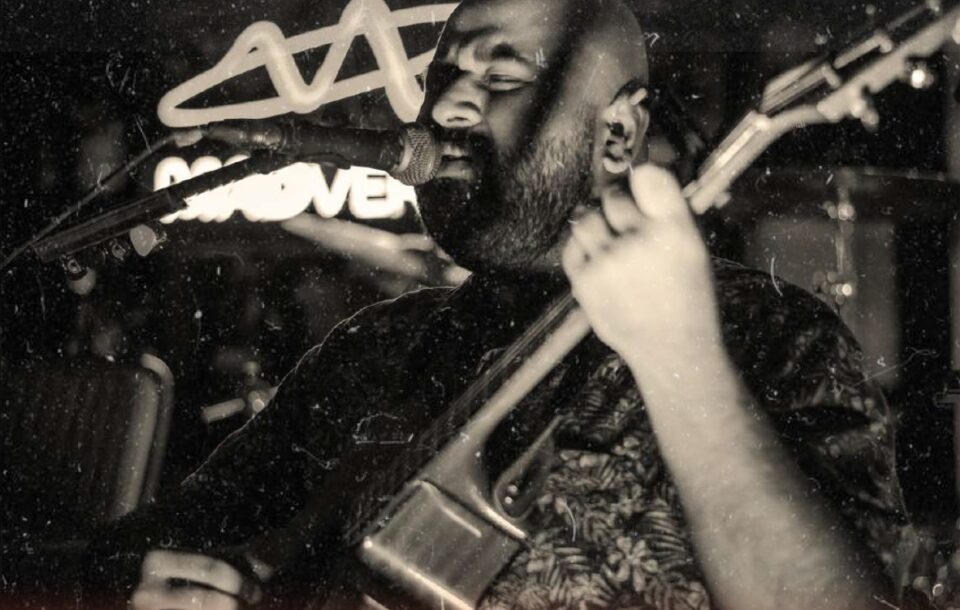 Black and white photo of Shourya Malhotra singing into a mic while playing guitar