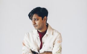 Mumbai singer-songwriter Tejas wearing white jacket and a red tshirt with arms crossed