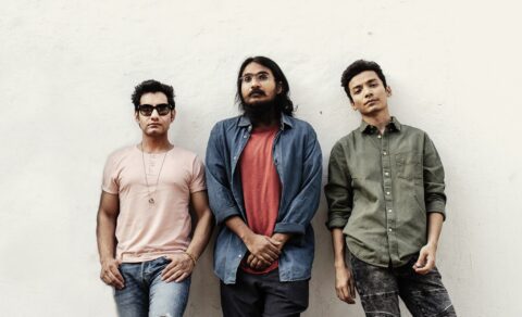 Band members of The Local Train leaning on a wall and posing for a photo