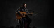 Sahitya Nepal Yaatri artist wearing black outfit, sitting and playing acoustic guitar