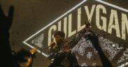 100 RBH live at a concert raising his hand with a mic with Gully Gang logo background