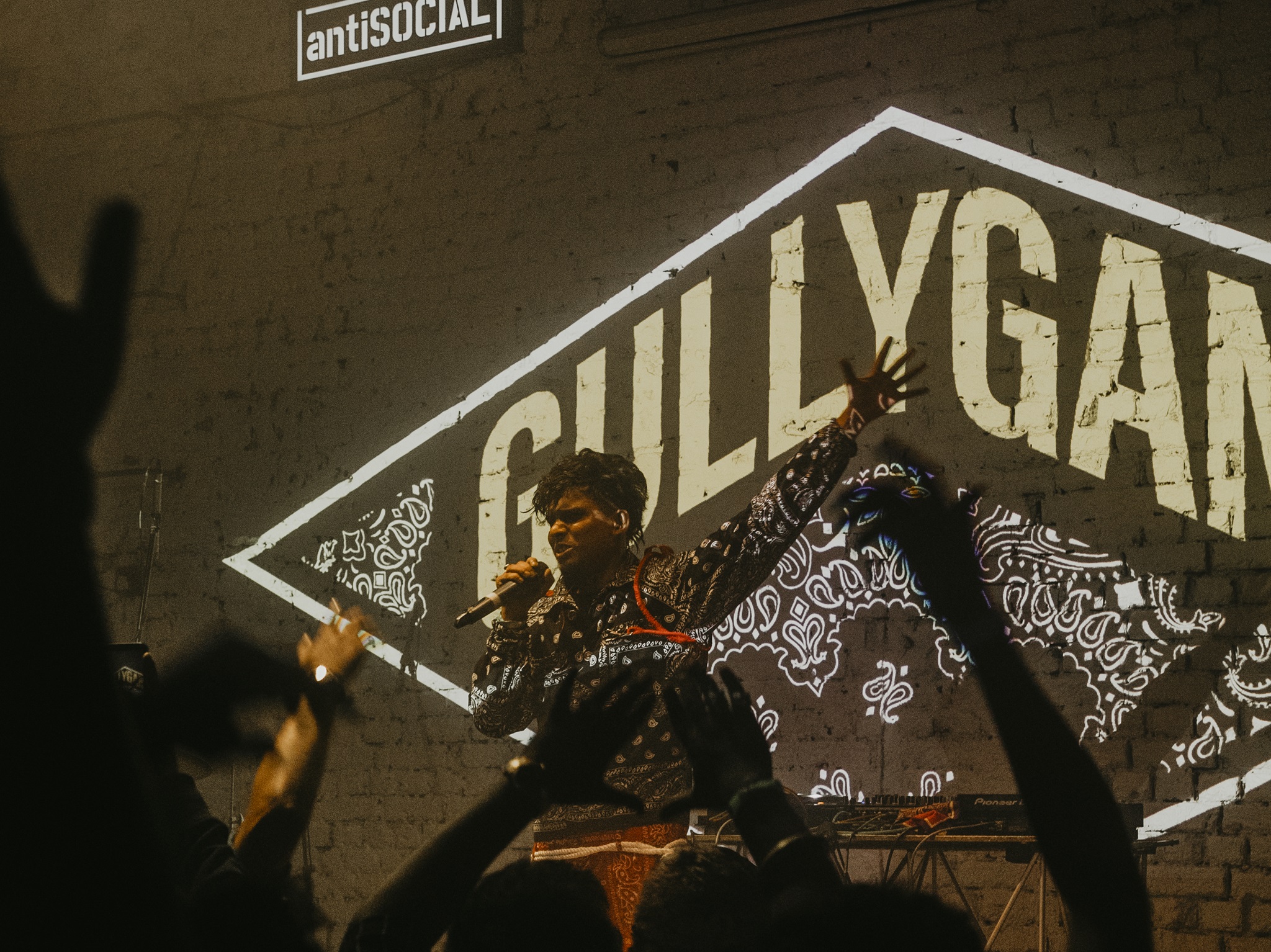 100 RBH live at a concert raising his hand with a mic with Gully Gang logo background