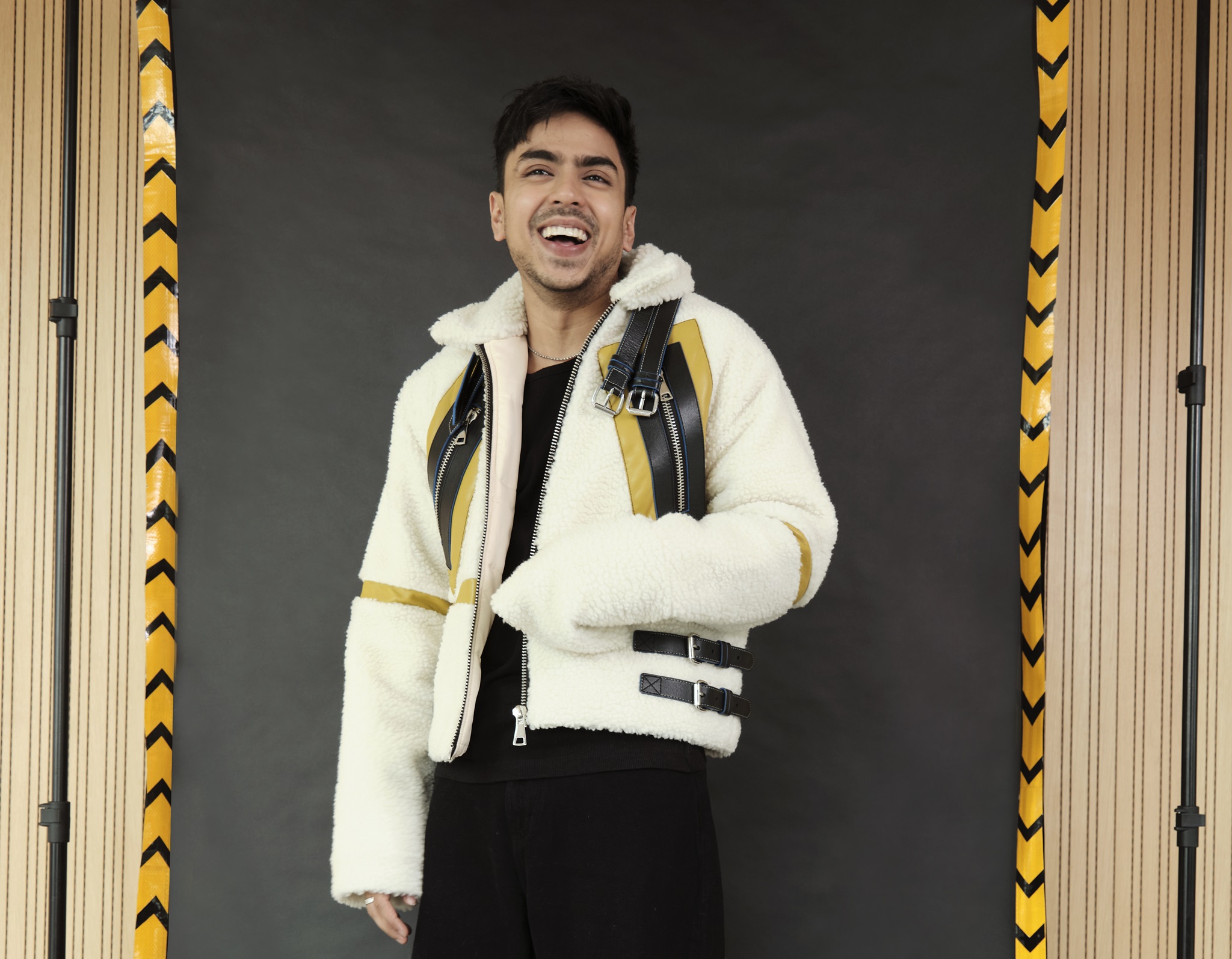 Actor Adarsh Gourav smiling, wearing an oversized white jacket and black trousers